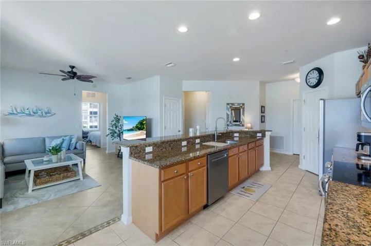 Open-concept living space featuring a kitchen island with granite countertops, wood cabinetry, and stainless steel appliances