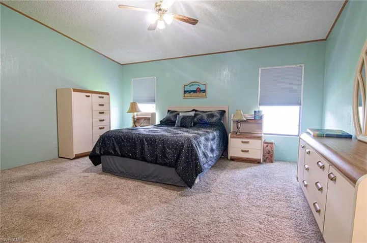 Carpeted bedroom featuring a ceiling fan, ornamental molding, and a textured ceiling