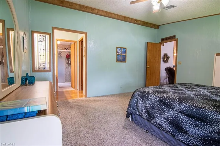 Bedroom featuring carpet, a textured ceiling, ensuite bath, ceiling fan, and visible vents