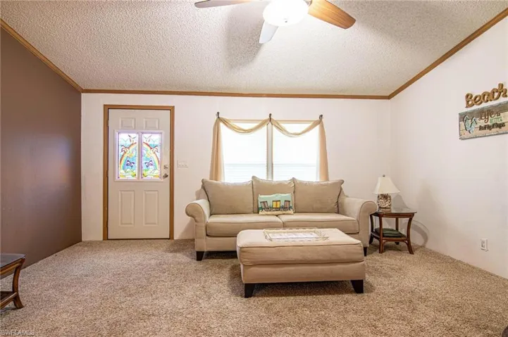 Living area with crown molding, carpet floors, a ceiling fan, a textured ceiling, and lofted ceiling