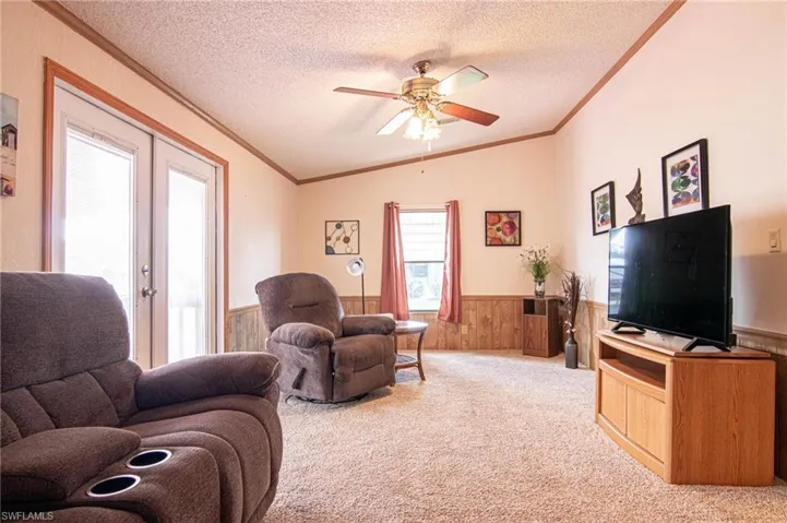 Carpeted living area featuring a textured ceiling, a ceiling fan, wainscoting, and ornamental molding
