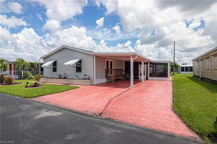 Manufactured / mobile home featuring a front lawn, an attached carport, decorative driveway, and a sunroom