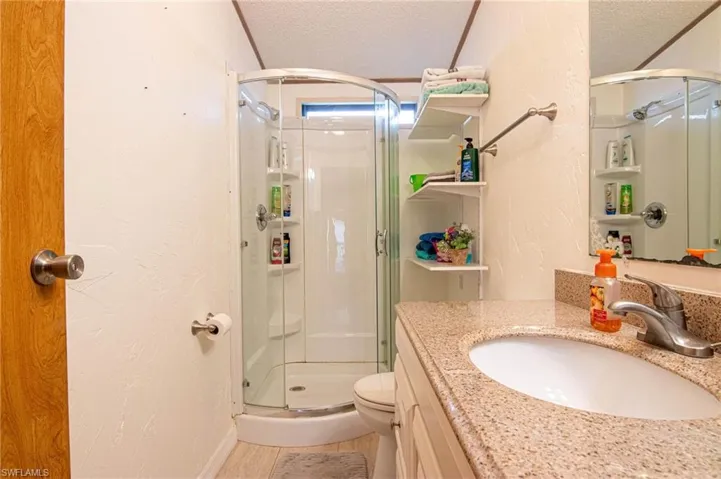 Full bath with vanity, toilet, a textured wall, a textured ceiling, and a stall shower