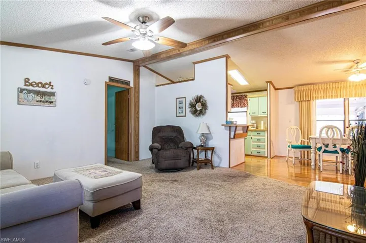 Living room featuring a textured ceiling, vaulted ceiling, ornamental molding, and a ceiling fan