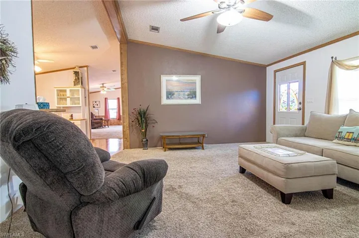 Carpeted living area featuring visible vents, lofted ceiling, ceiling fan, and a textured ceiling