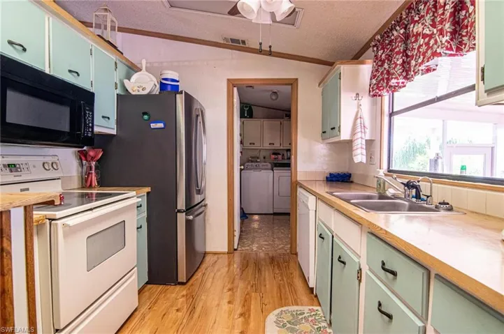 Kitchen with vaulted ceiling, a sink, separate washer and dryer, white appliances, and visible vents