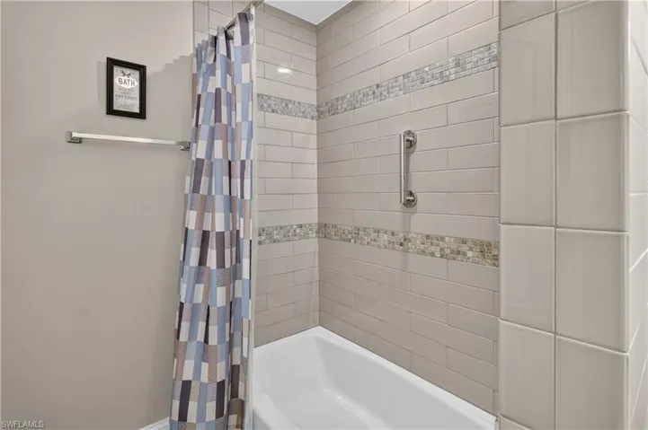 White bathtub with subway tile surround, mosaic accent bands, and a chrome grab bar