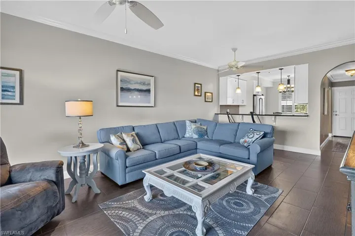Spacious living area featuring dark wood-finish flooring, crown molding, and a ceiling fan