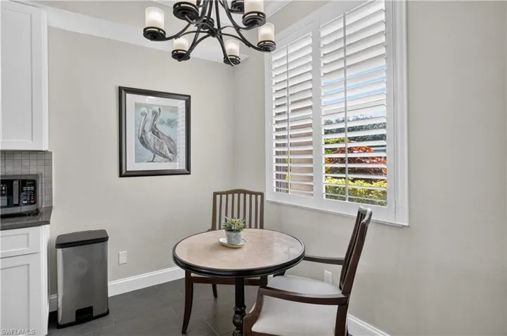 Breakfast nook featuring a large window with white plantation shutters, dark gray tile flooring, and a contemporary chandelier