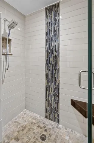 Tiled shower with a vertical mosaic accent stripe, subway tile walls, and a built-in corner bench