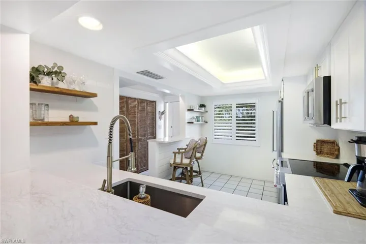 Kitchen with light tile patterned floors, sink, a tray ceiling, and white cabinetry