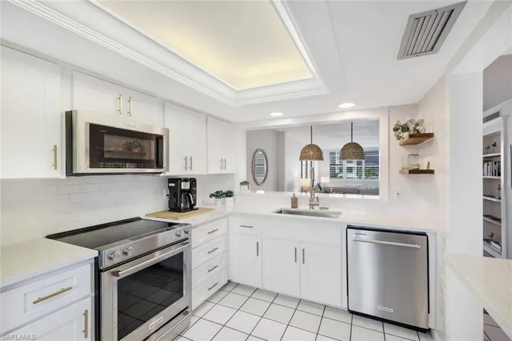 Kitchen with tasteful backsplash, a raised ceiling, stainless steel appliances, white cabinetry, and sink