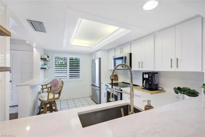 Kitchen featuring white cabinetry, kitchen peninsula, light tile patterned flooring, a tray ceiling, and stainless steel appliances