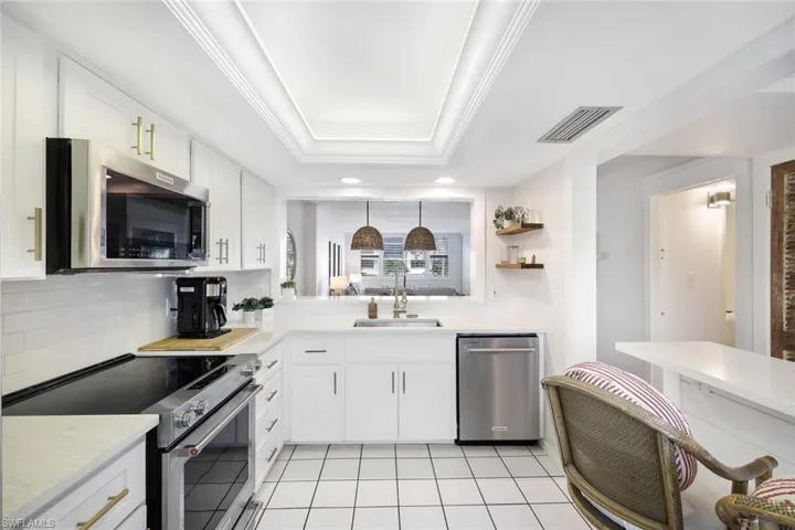 Kitchen with a raised ceiling, appliances with stainless steel finishes, white cabinets, light tile patterned floors, and sink
