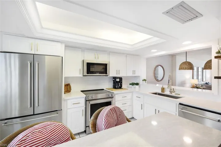 Kitchen featuring stainless steel appliances, sink, tasteful backsplash, white cabinetry, and a raised ceiling
