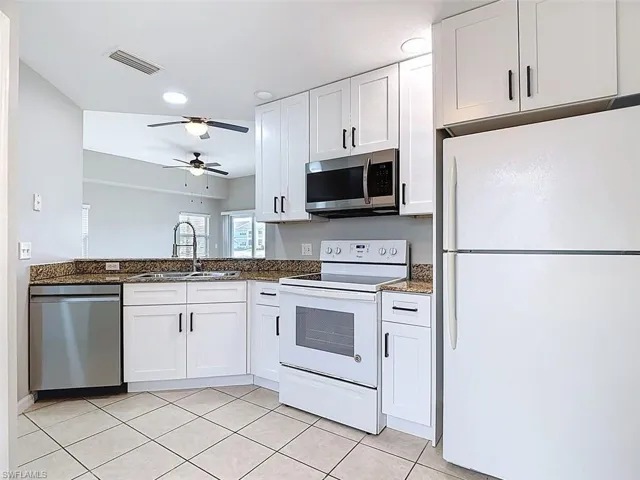 Kitchen featuring stainless steel appliances, white cabinets, dark stone counters, light tile patterned floors, and recessed lighting