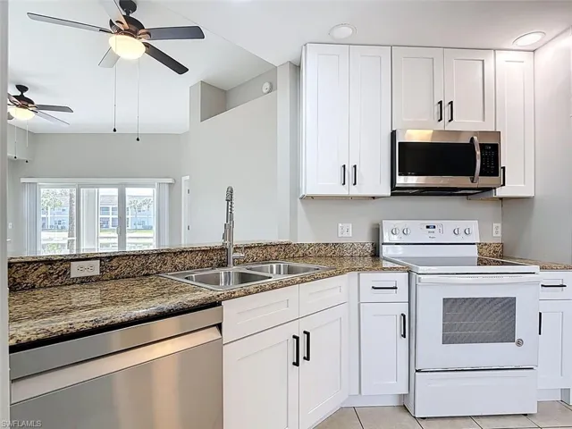 Kitchen featuring stainless steel appliances, white cabinets, ceiling fan, dark stone countertops, and light tile patterned flooring