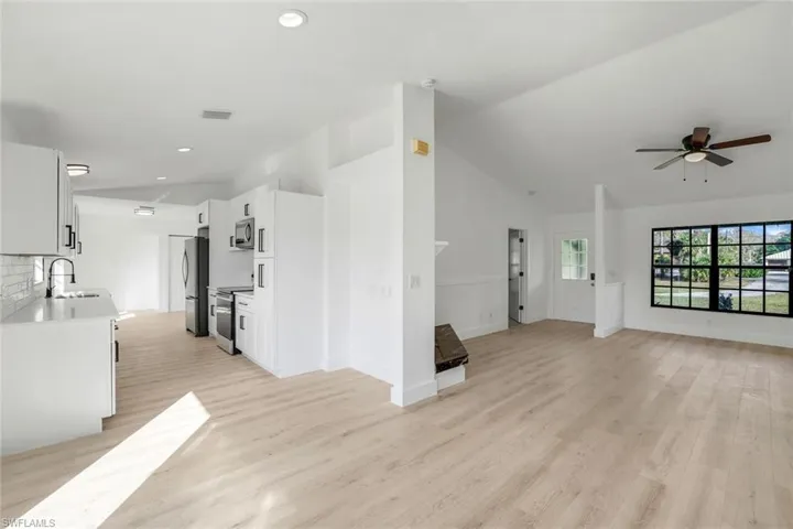 Unfurnished living room featuring ceiling fan, lofted ceiling, sink, and light hardwood / wood-style floors