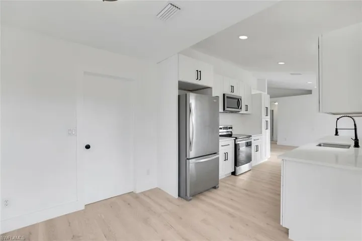 Kitchen with sink, white cabinetry, tasteful backsplash, light wood-type flooring, and stainless steel appliances