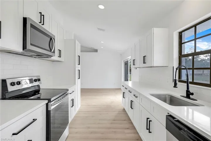 Kitchen with stainless steel appliances, white cabinetry, sink, and light wood-type flooring