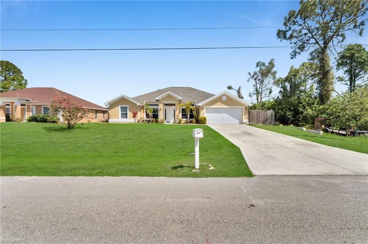 View of front facade featuring an attached garage, concrete driveway, fence, and a front lawn