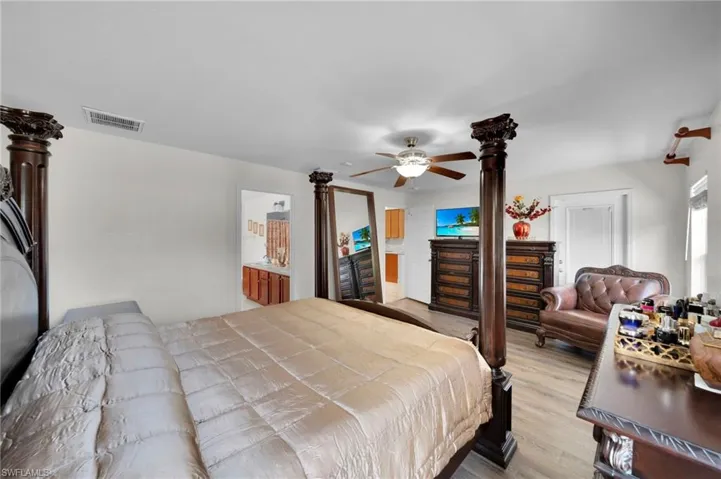 Bedroom featuring light wood-type flooring, a ceiling fan, visible vents, and connected bathroom