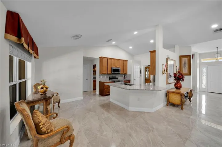 Kitchen featuring vaulted ceiling, light stone counters, backsplash, stainless steel appliances, and a sink