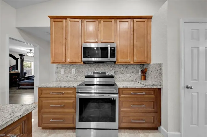 Kitchen with brown cabinetry, decorative backsplash, light stone counters, and stainless steel appliances
