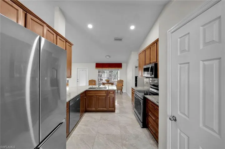 Kitchen with light stone counters, recessed lighting, a peninsula, brown cabinetry, and stainless steel appliances