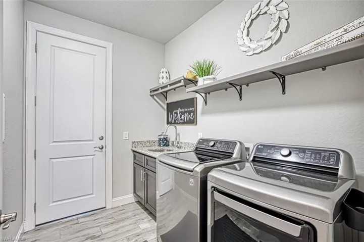 Clothes washing area featuring cabinets, sink, washer and clothes dryer, and light hardwood / wood-style flooring