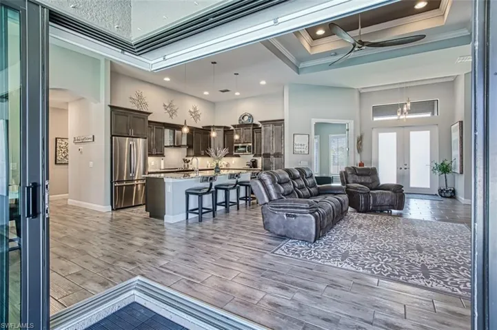 Tiled living room featuring french doors, ornamental molding, ceiling fan with notable chandelier, a towering ceiling, and a raised ceiling