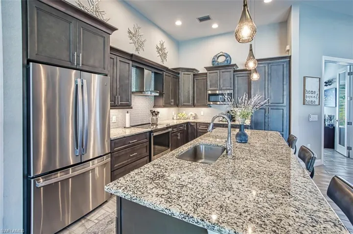 Kitchen with wall chimney range hood, backsplash, a breakfast bar area, appliances with stainless steel finishes, and sink