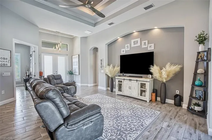 Living room with ceiling fan, a raised ceiling, crown molding, light wood-type flooring, and french doors