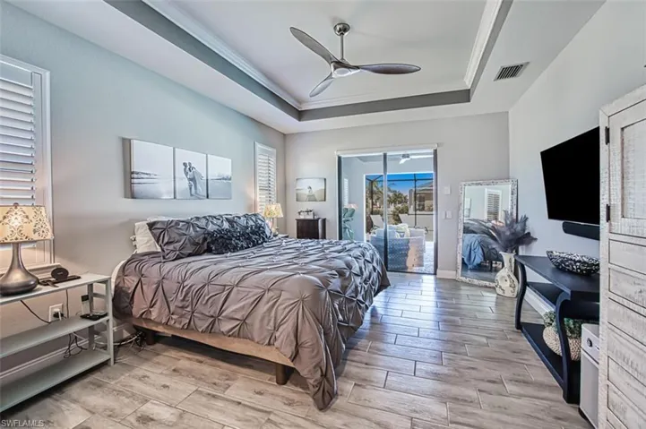 Bedroom with access to outside, light wood-type flooring, ceiling fan, and a raised ceiling
