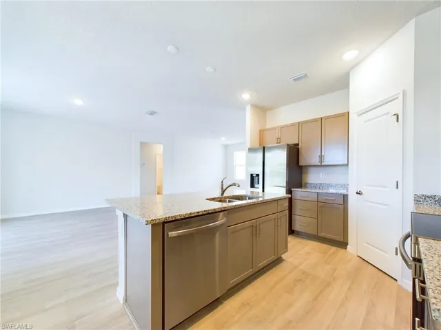 Kitchen featuring light wood-type flooring, a kitchen island with sink, light stone counters, sink, and stainless steel appliances