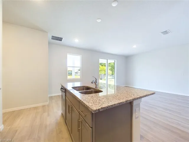 Kitchen with light wood-type flooring, stainless steel dishwasher, a kitchen island with sink, light stone countertops, and sink