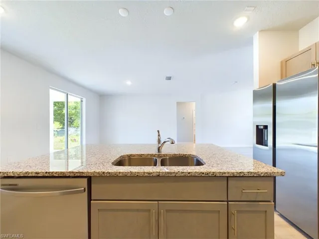 Kitchen with sink, light stone counters, an island with sink, and stainless steel appliances