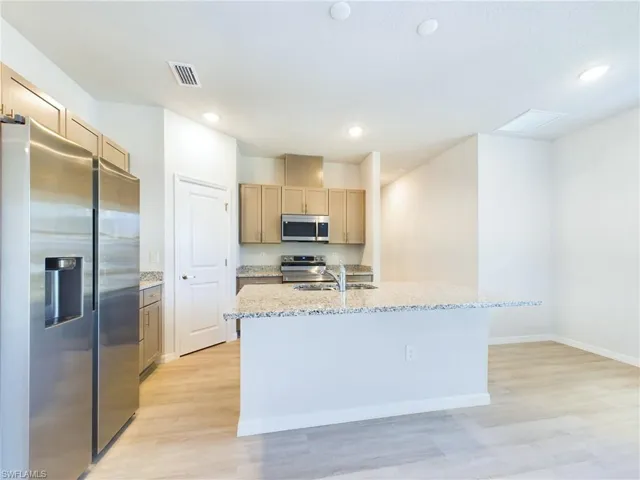 Kitchen featuring stainless steel appliances, a center island with sink, light stone countertops, and light hardwood / wood-style flooring