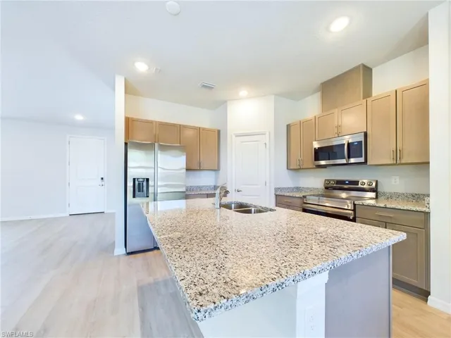 Kitchen with light wood-type flooring, a kitchen island with sink, light stone countertops, sink, and stainless steel appliances
