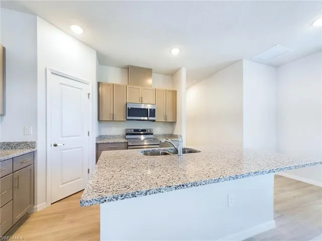 Kitchen with light wood-type flooring, stainless steel appliances, light stone countertops, and an island with sink