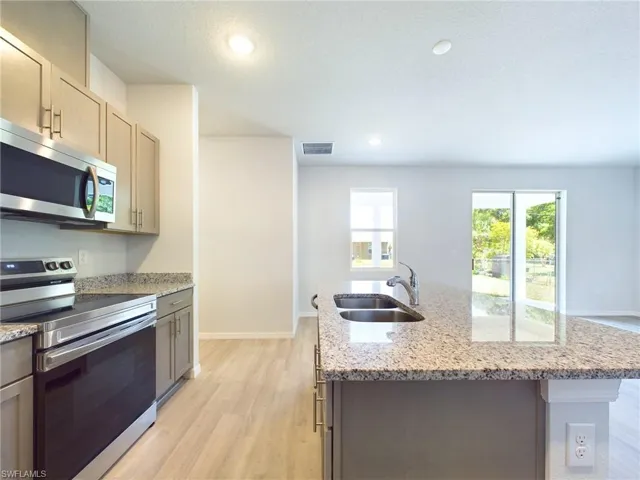 Kitchen with light wood-type flooring, sink, stainless steel appliances, and an island with sink