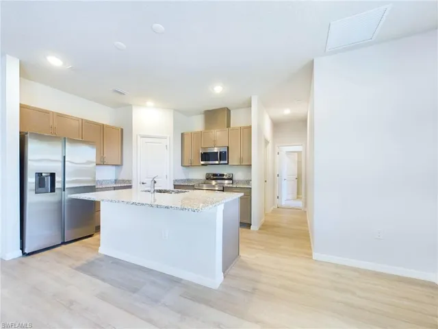 Kitchen featuring light wood-type flooring, light stone countertops, sink, a center island with sink, and stainless steel appliances
