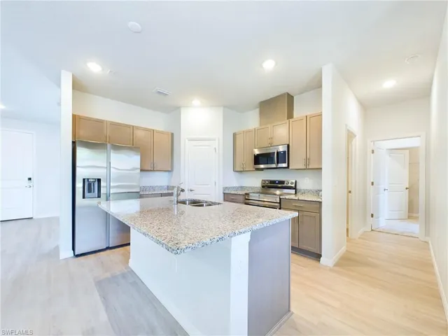 Kitchen with light hardwood / wood-style flooring, a kitchen island with sink, light stone counters, sink, and stainless steel appliances