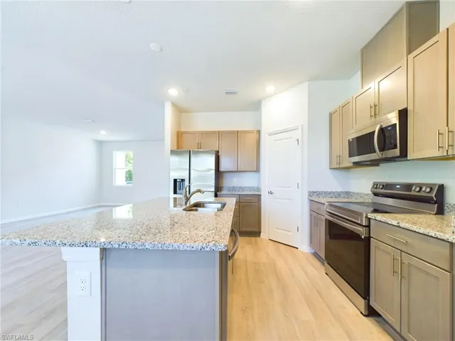 Kitchen with appliances with stainless steel finishes, light stone countertops, light hardwood / wood-style floors, sink, and a center island with sink