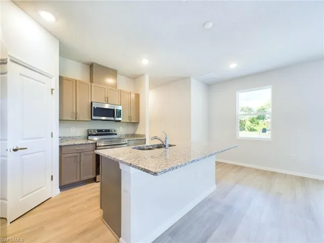 Kitchen featuring light wood-type flooring, stainless steel appliances, a center island with sink, and light stone countertops
