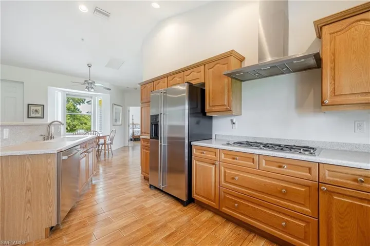 Kitchen featuring light hardwood / wood-style flooring, ceiling fan, wall chimney exhaust hood, stainless steel appliances, and sink