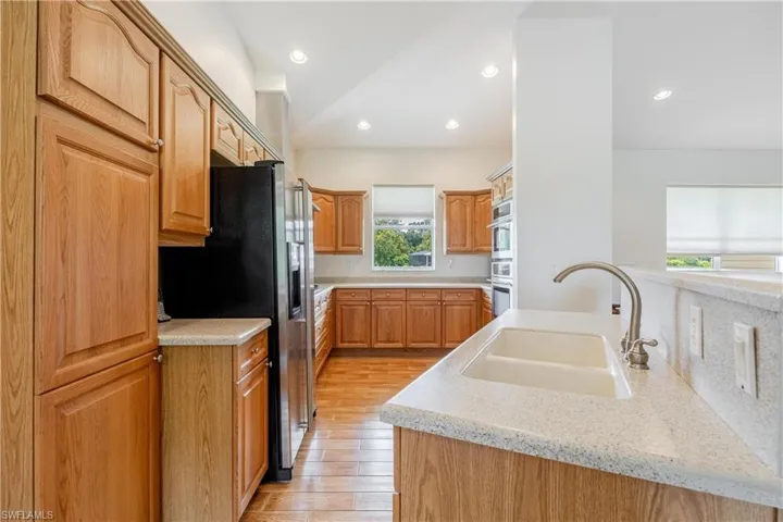 Kitchen featuring double oven, fridge with ice dispenser, light stone countertops, light hardwood / wood-style flooring, and sink