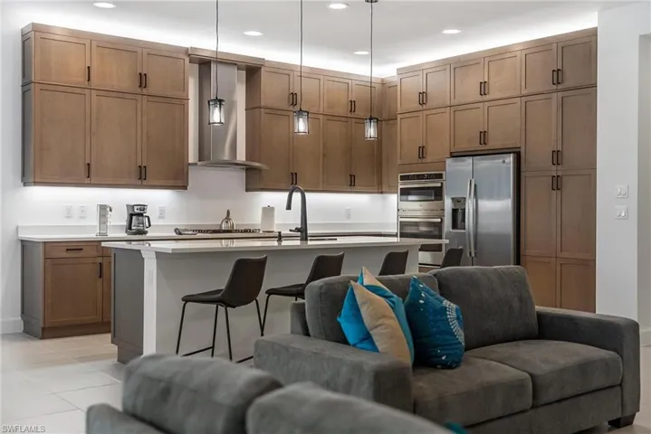Kitchen with appliances with stainless steel finishes, a breakfast bar, hanging light fixtures, an island with sink, and wall chimney exhaust hood