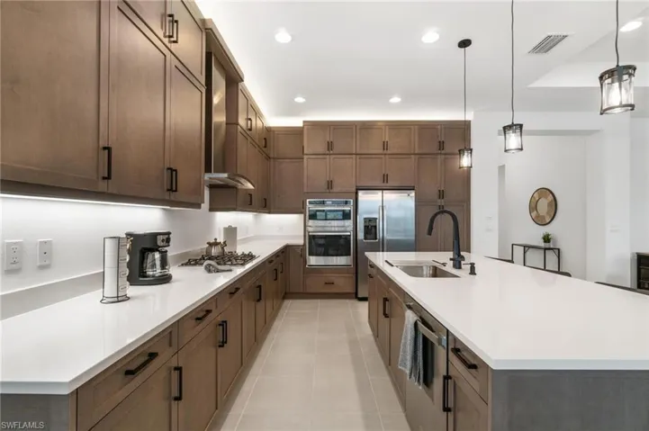 Kitchen featuring light tile patterned floors, appliances with stainless steel finishes, sink, pendant lighting, and a center island with sink