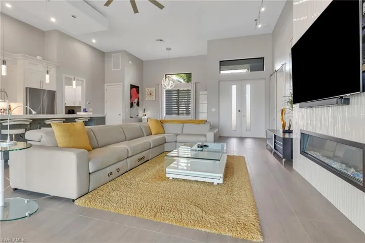Living room with a towering ceiling, a glass covered fireplace, light tile patterned flooring, recessed lighting, and a ceiling fan